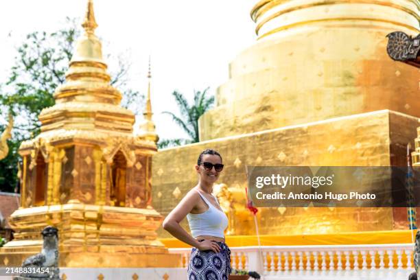 young woman posing next to the pagoda at wat phra singh temple in chang mai. - singh stock pictures, royalty-free photos & images