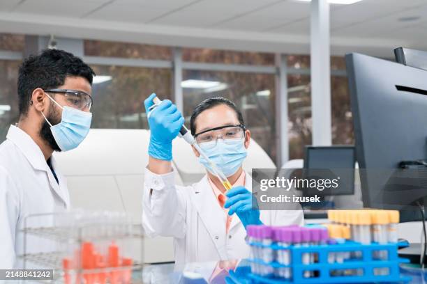 female scientist wearing face mask while pipetting chemical in test tube at laboratory - safety glasses stock pictures, royalty-free photos & images