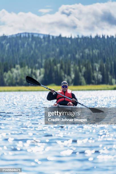 man kayaking in lake against trees under cloudy sky - northern europe stock pictures, royalty-free photos & images