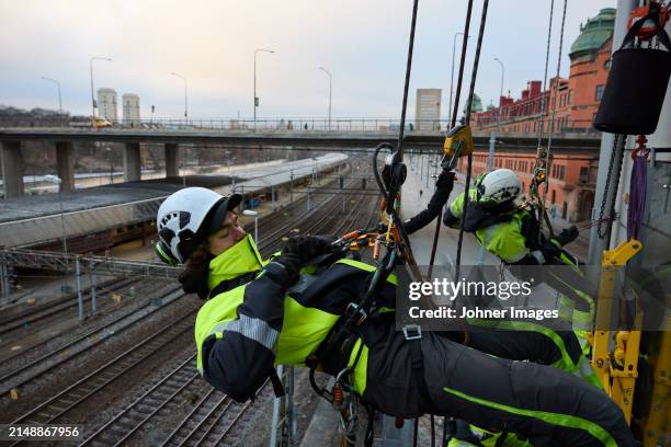 rope access worker fastening carabiner to rope while hanging from building - karabiner stock pictures, royalty-free photos & images