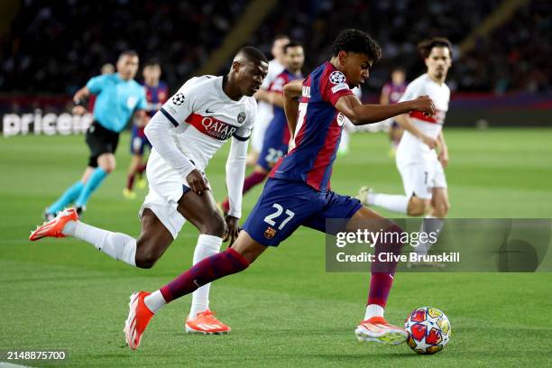 Lamine Yamal of FC Barcelona runs with the ball whilst under pressure from Nuno Mendes of Paris Saint-Germain during the UEFA Champions League...