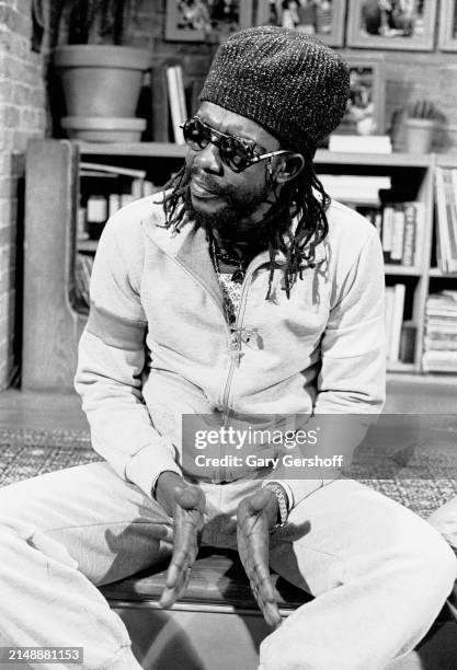 View of Jamaican Reggae musician Peter Tosh seated on a low stage during an interview at MTV Studios, New York, New York, May 19, 1983.