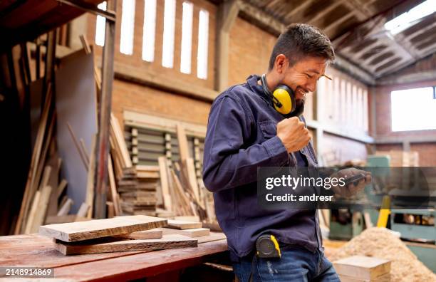 worker at a lumberyard receiving good news on his cell phone - good news stock pictures, royalty-free photos & images