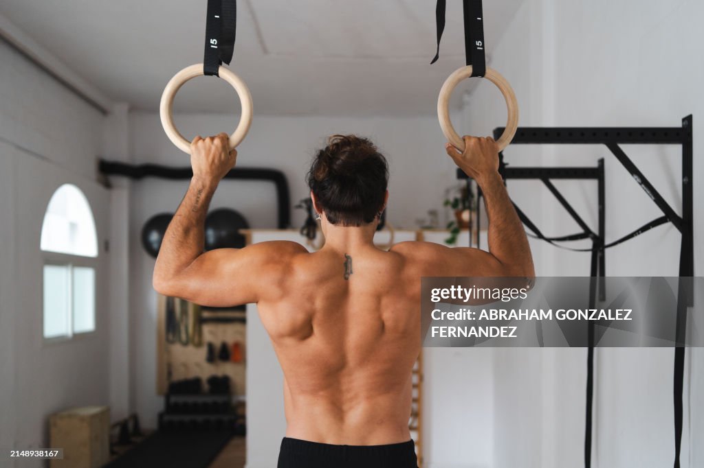 Strong man hanging from gymnastic rings indoors