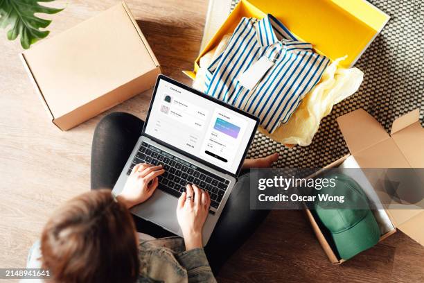 young woman doing online shopping with laptop sitting on the floor at home - accro du shopping photos et images de collection