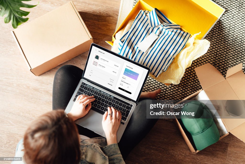 Young woman doing online shopping with laptop sitting on the floor at home