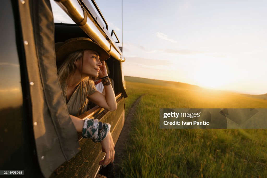 Carefree female tourist during game drive trough wilderness at sunset.