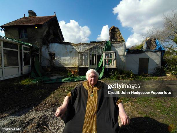 English film director and photographer Ken Russell seated outside his fire damaged cottage in the village of East Boldre in the New Forest area of...