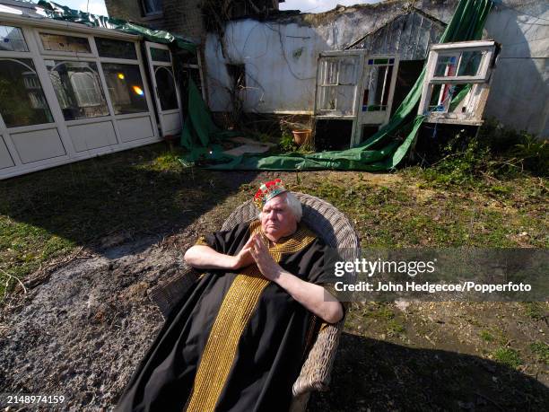 English film director and photographer Ken Russell seated outside his fire damaged cottage in the village of East Boldre in the New Forest area of...