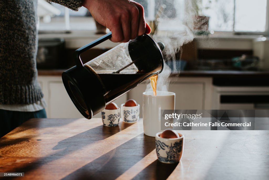 A man pours a cup of coffee from a french press coffee maker