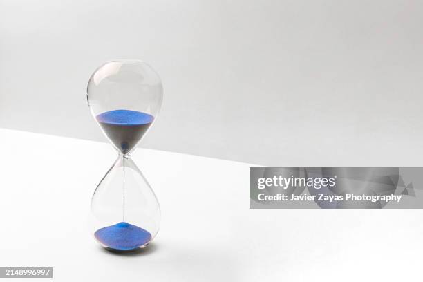 blue colored sand hourglass on bright white background - wartezeit stock-fotos und bilder
