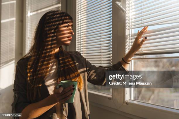 side portrait of a woman looking through a window - jaloezie negatieve emotie stockfoto's en -beelden