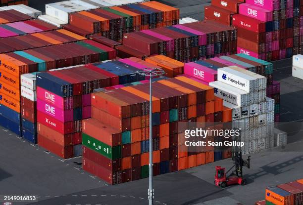 In this aerial view a freight-carrying vehicle called a straddle carrier, or straddle truck, drives among stacked shipping containers at Hamburg Port...