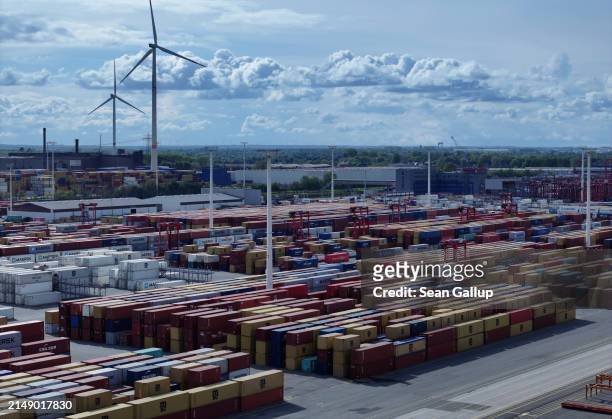 In this aerial view shipping containers lie stacked at Hamburg Port as wind turbines spin behind on April 17, 2024 in Hamburg, Germany. The...