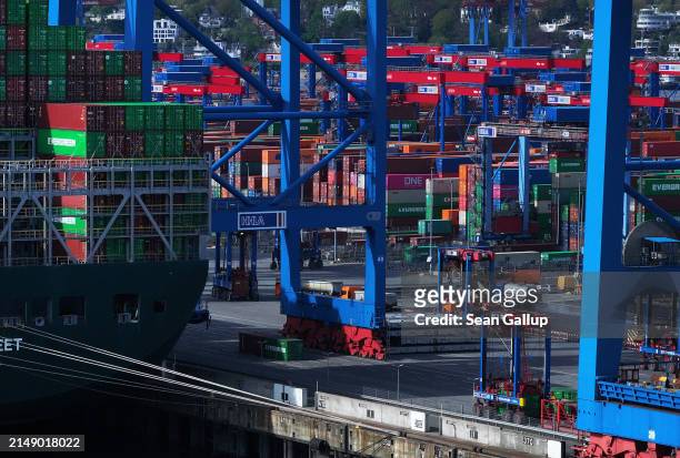 In this aerial view freight-carrying vehicles called straddle carriers, or straddle trucks, drive among stacked shipping containers and a cargo ship...