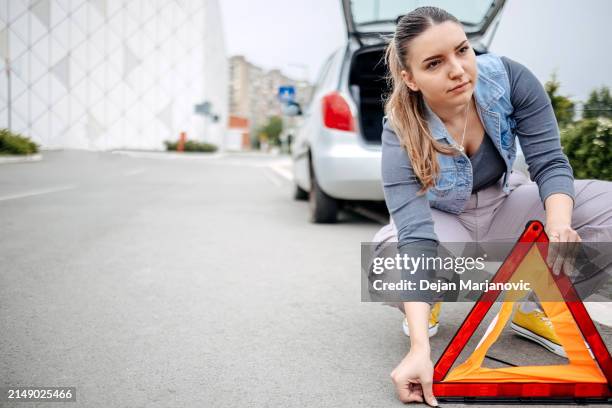 woman preparing to change a flat tyre putting a safety sign on the road - spare tyre stock pictures, royalty-free photos & images