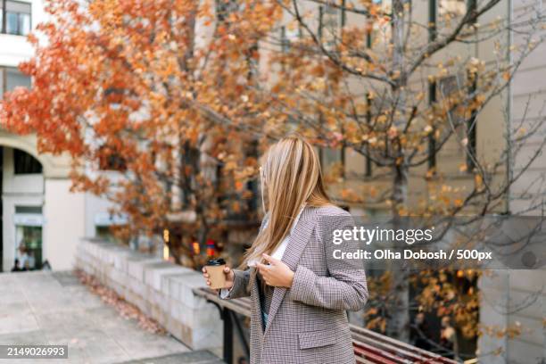 young woman using mobile phone while standing against trees during autumn - peel park stock pictures, royalty-free photos & images