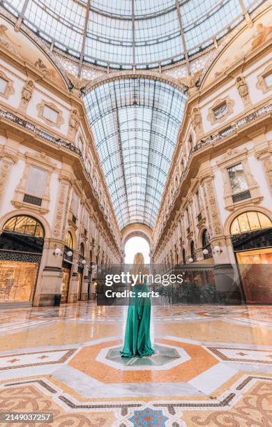 una giovane turista in un abito lungo verde che cammina, fa shopping e si trova nella galleria vittorio emanuele ii a milano, in italia, offre una vista mozzafiato della porta d'oro dello shopping di lusso - moda foto e immagini stock
