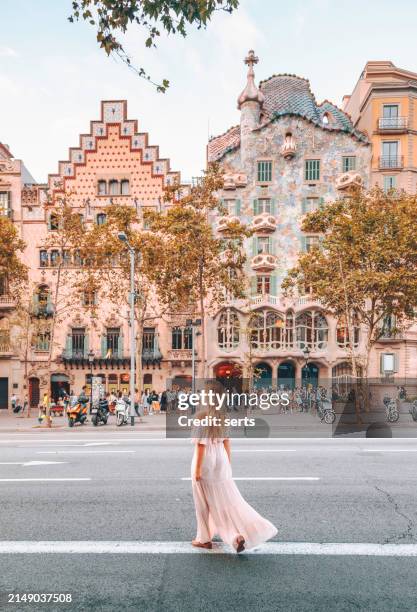 a young tourist woman in pink long dress having fun walking on the streets of barcelona and on the road on a sunny day with the characteristic buildings of barcelona in the background and the famous casa batlló of antonio gaudí in catalonia, spain - casa spain stock pictures, royalty-free photos & images