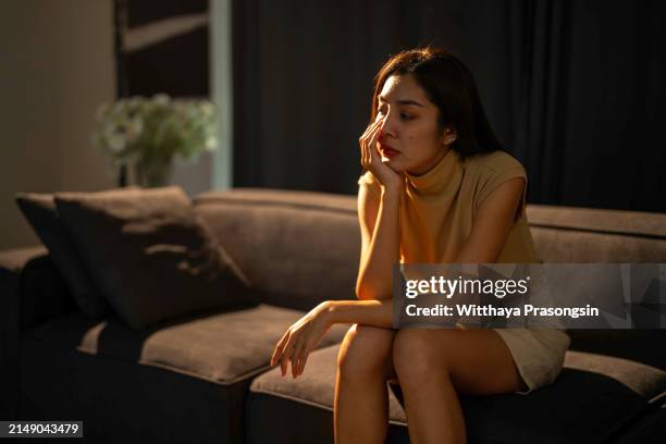 sad woman sitting on couch alone at home - ruptura sentimental fotografías e imágenes de stock