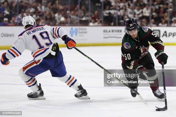 Sean Durzi of the Arizona Coyotes skates with the puck against Adam Henrique of the Edmonton Oilers during the second period of the NHL game at...