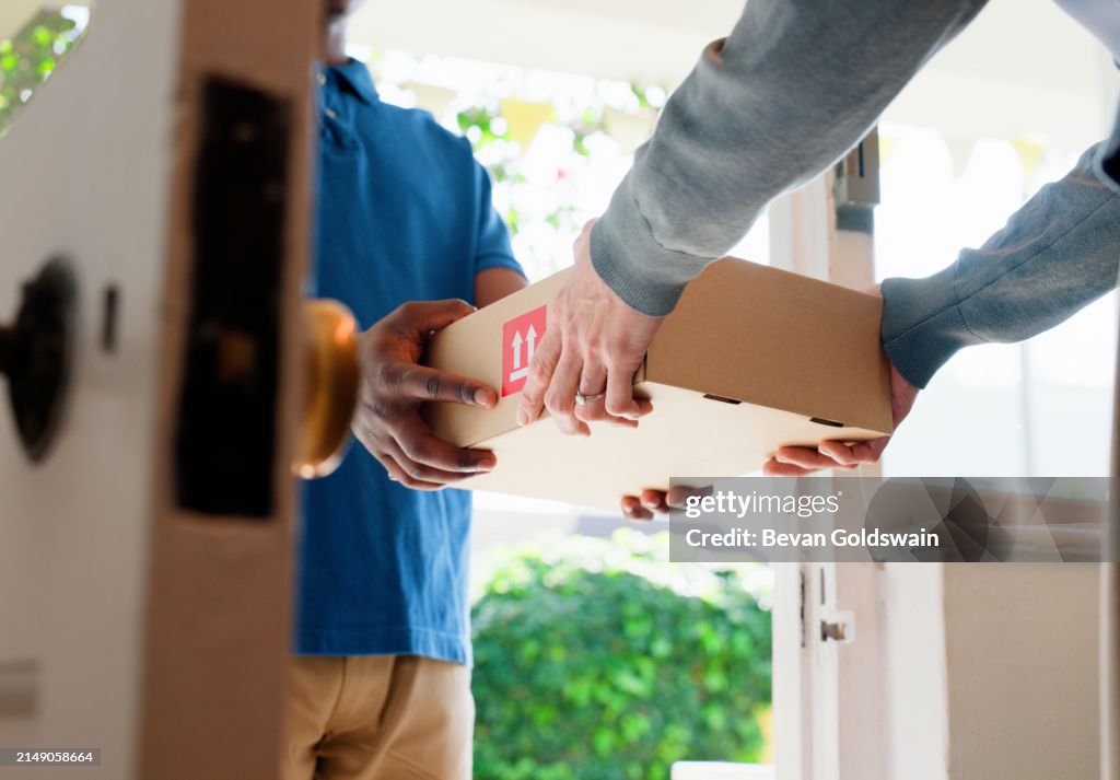 Hands, box and delivery man at front door in home with client, services and shipping for commercial product. People, courier and cardboard package for supply chain, logistics or distribution at house