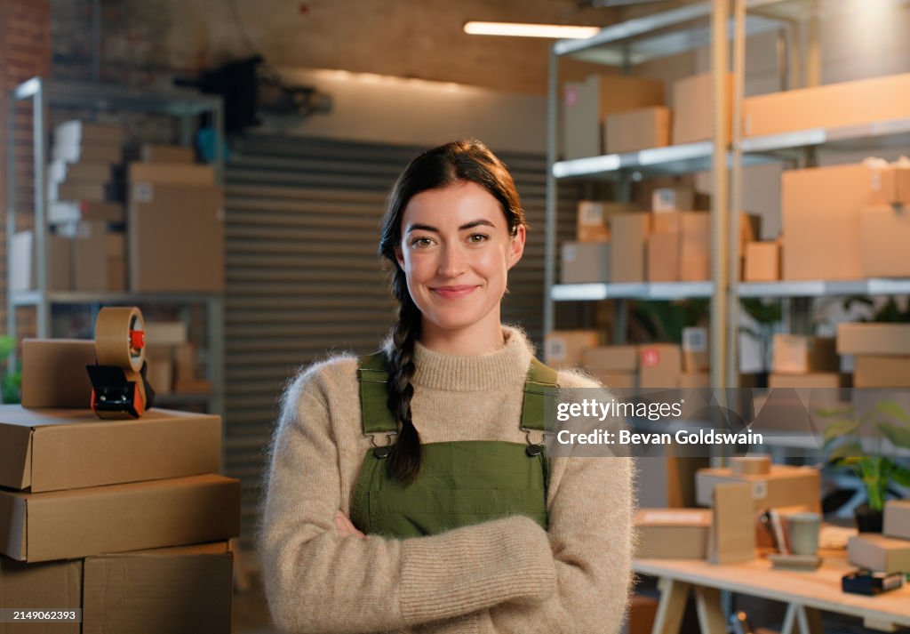Logistik, verschränkte Arme und Porträt einer Unternehmerin mit einem kleinen Unternehmen in der E-Commerce-Branche. Lächeln, Stolz und selbstbewusste weibliche Person im Lager mit Kartons für den Frachtversand.