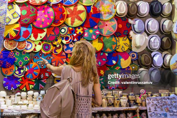 women standing in front of colorful woven baskets and bags on a market stall in the souk in aswan, egypt - aswan stock pictures, royalty-free photos & images