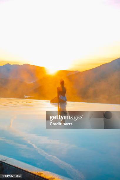 eine junge frau steht am rand des infinity-pools und genießt den blick auf den sonnenuntergang und das entspannen am pool mit blick auf die naturlandschaft in den dolomiten, italien - spiegelteich stock-fotos und bilder