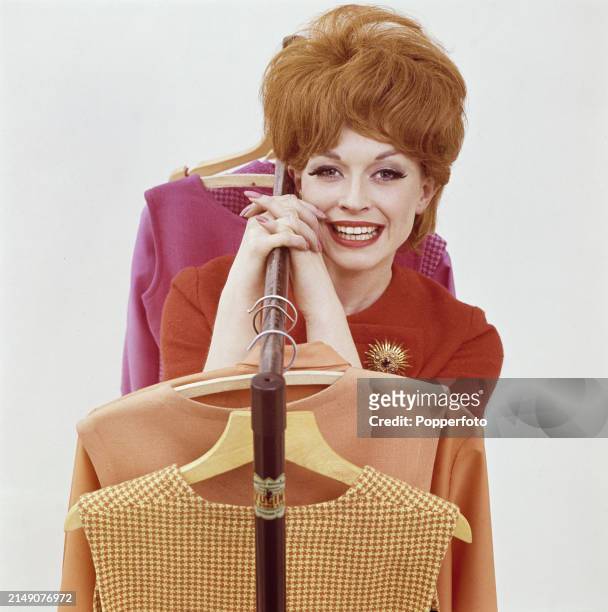 Posed studio portrait of female fashion model Suzie posed with a rail of flattering outfits for the new season, she wears a short sleeved red wool...