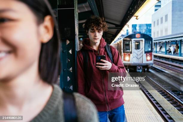 young gen-z man on the subway platform waiting for the commuter train. man is using smart phone - dichterbij komen stockfoto's en -beelden