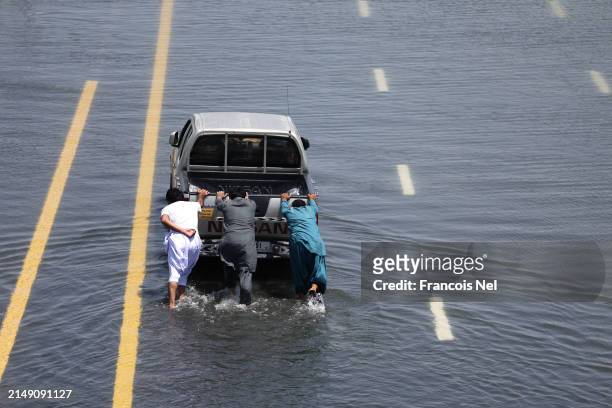 People push a stalled car on a flooded highway on April 18, 2024 in Dubai, United Arab Emirates. Atypically heavy rains in the UAE on Monday and...