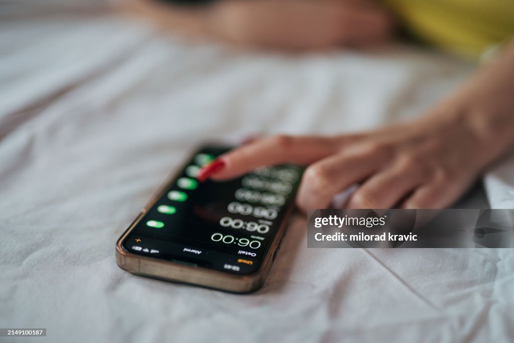 Eine junge Frau schaltet morgens einen Wecker auf ihrem Handy aus