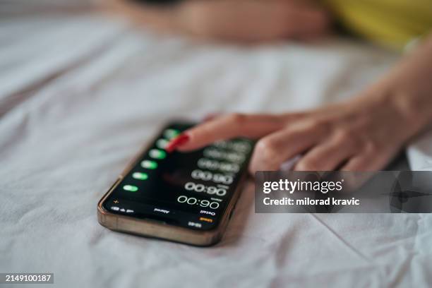 a young woman snooze an alarm on her phone in the morning - alarm stockfoto's en -beelden