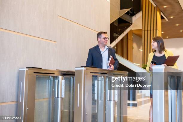 a businessman and a businesswoman dressed in business casual are talking in a business building. - entrance gate stock pictures, royalty-free photos & images