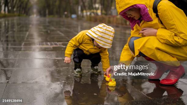 美しい面白いブロンドの幼児の男の子とゴムのアヒルの遊びの雨 - レインコート ストックフォトと画像
