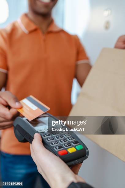 a young man accepts the order from the courier and uses the payment terminal with a contactless credit card - creditcardlezer stockfoto's en -beelden