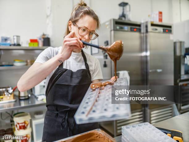 eine chocolatierin bei der arbeit in der schokoladenfabrik - süßwarengeschäft stock-fotos und bilder