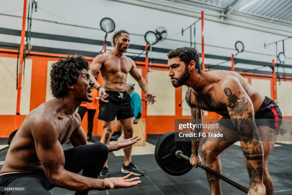 Friends motivating young man doing weightlifting at gym
