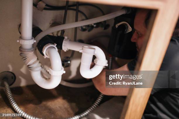 man working on plumbing under kitchen sink - under sink stock pictures, royalty-free photos & images