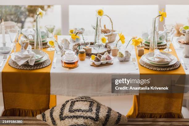 setting table for easter dinner with candles, flowers, multicolored eggs and ceramic plates in shape easter bunny. - easter breakfast stock pictures, royalty-free photos & images