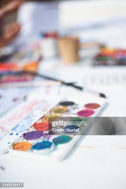 close-up of a palette with assorted watercolour paints on a table with a paintbrush and paper - palet stockfoto's en -beelden