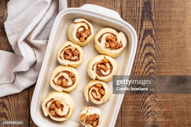 baking cinnamon rolls with apples in baking dish on rustic wooden table - apple cinnamon stock pictures, royalty-free photos & images