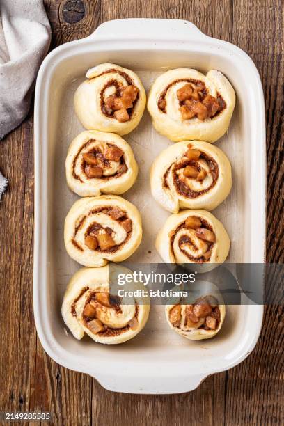 baking cinnamon rolls with apples in baking dish on rustic wooden table - cake tin stock pictures, royalty-free photos & images
