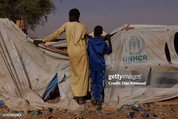 Two boys peer over a UNHCR aid tent as newly arrived refugees from Darfur in Sudan, gather at a relocation camp near the border on April 19, 2024 in...