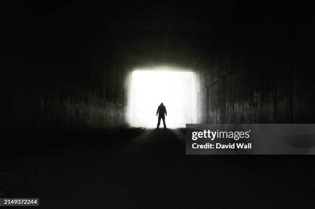 a scary hooded figure, standing at the entrance to a long dark tunnel - capuz imagens e fotografias de stock
