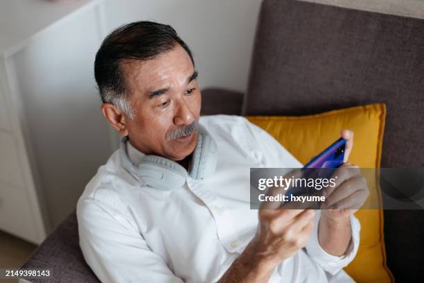 homme chinois asiatique senior jouant à un jeu mobile dans le salon - jeu mobile photos et images de collection