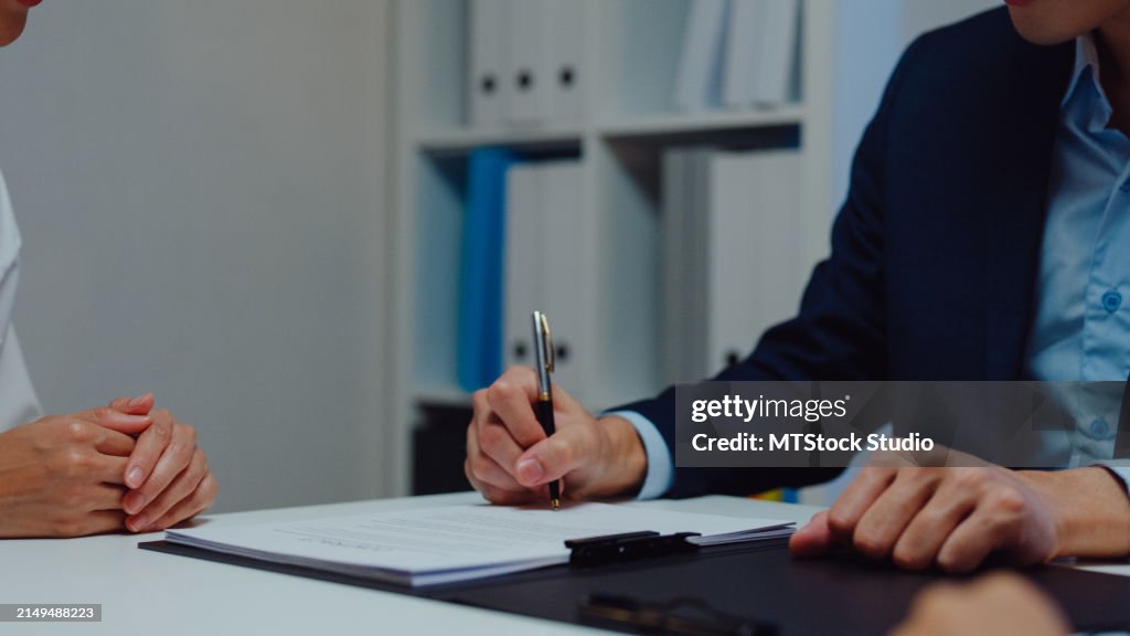 Closeup of young Asian businessman mentor corporate leader manager counselor communicate with businesswoman and sign a contract at office night. Businesspeople in workplace.
