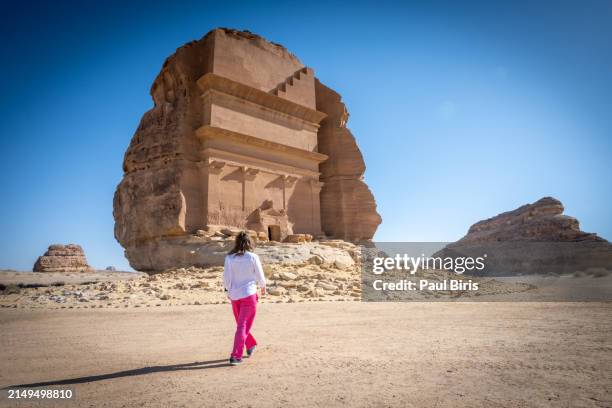 young caucasian woman in front tomb lihyan son of kuza or qasr al-farid at hegra, saudia arabia - punto de referencia natural fotografías e imágenes de stock