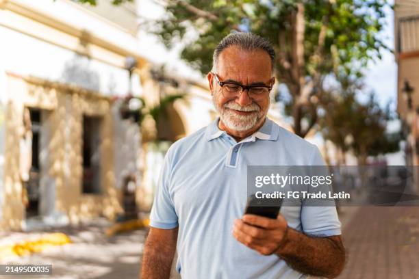 senior man walking and using mobile phone outdoors - old portable phone stock pictures, royalty-free photos & images